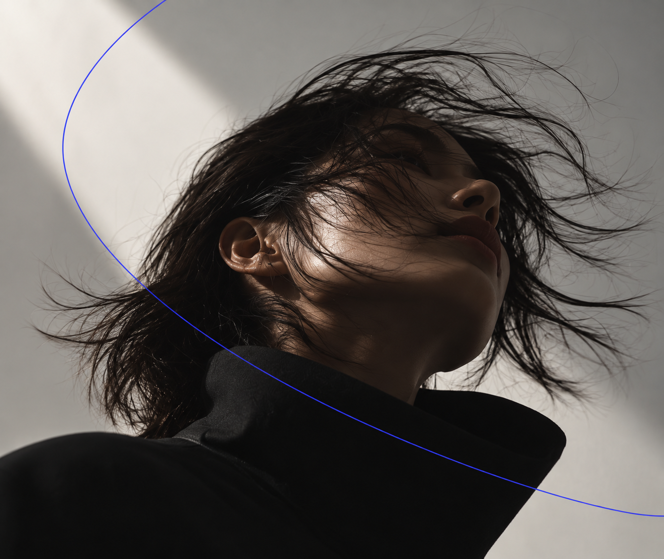 Portrait looking up, hair caught mid-motion, crossed by a thin blue line