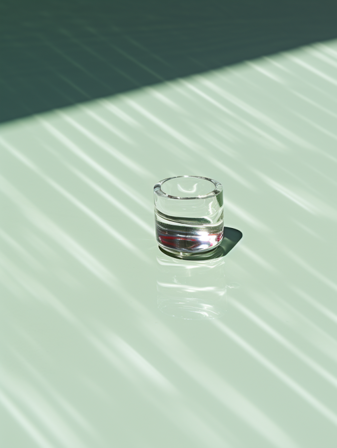 A single glass on a pale green surface striped with light